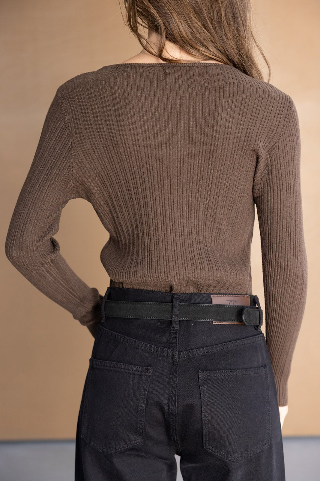 חולצת נשים סריג חום עם שרוולים ארוכים ומכנסי ג'ינס שחורים, צילום גב