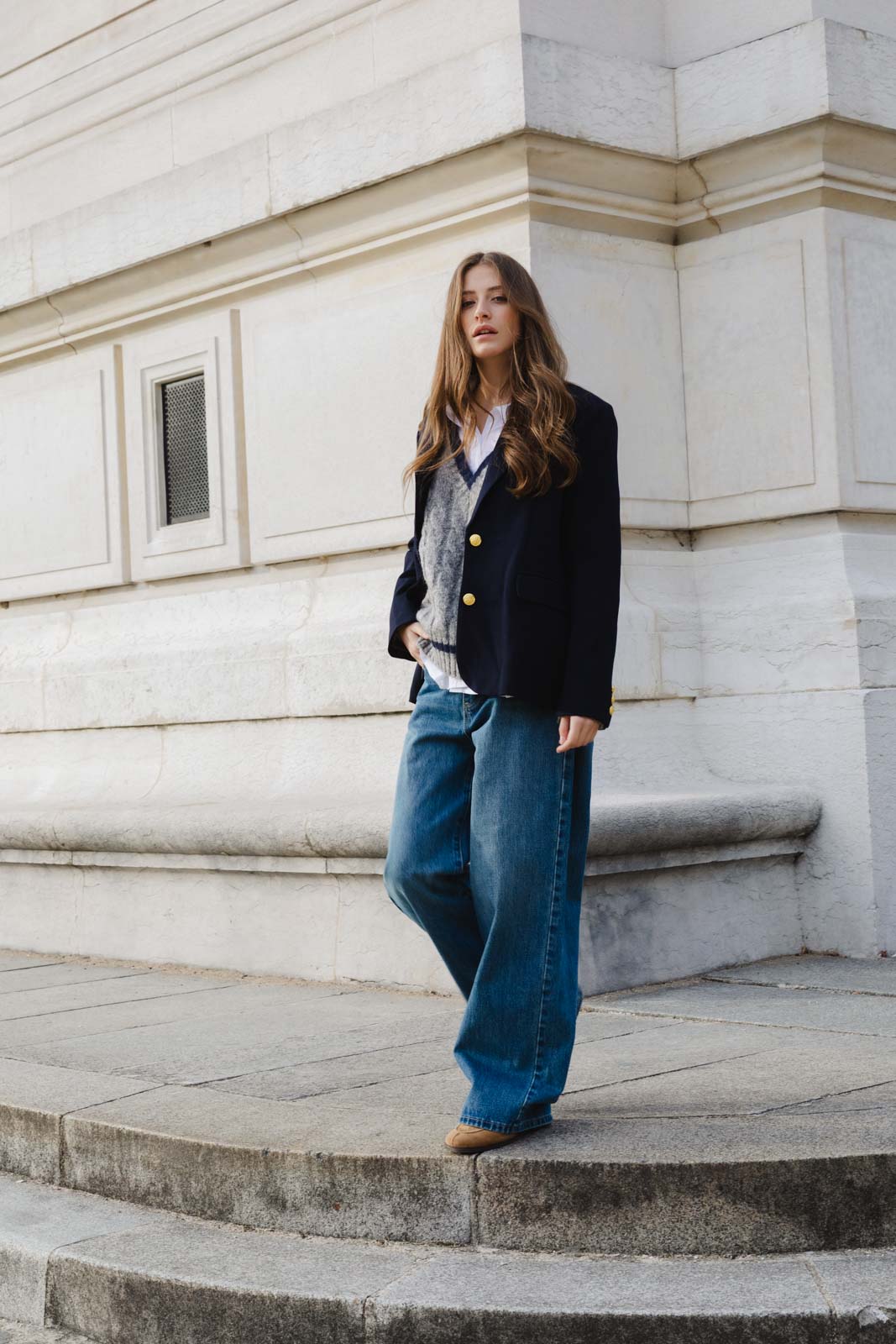 אופנת רחוב לנשים, דגם ג'קט כחול עם כפתורים, סוודר אפור ומכנסי ג'ינס רחבים, רקע עירוני קלאסי