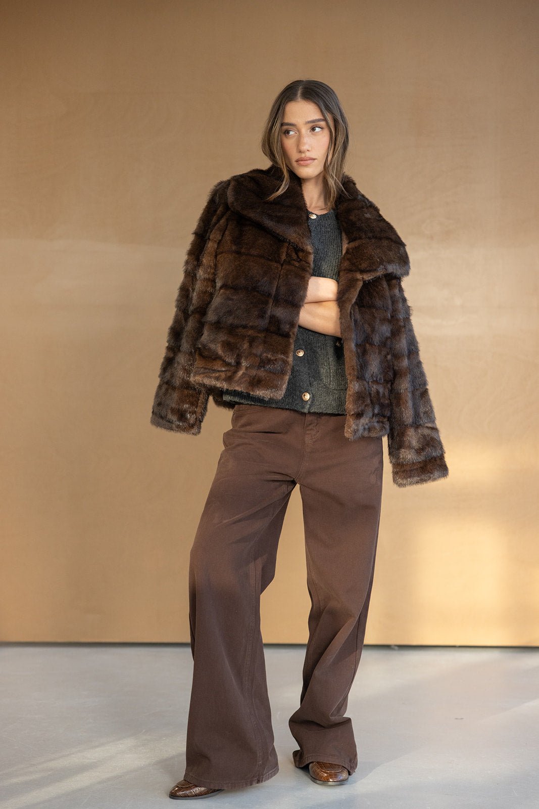 דוגמנית לובשת מעיל פרווה חום ומכנסיים רחבים חומים, אופנת חורף לנשים צעירות