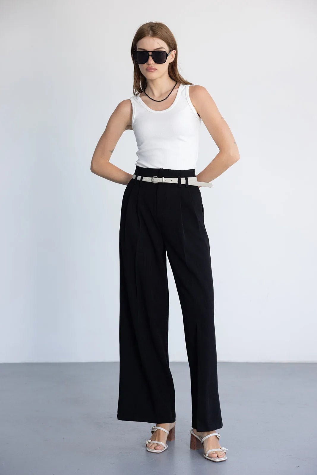 דוגמנית עם גופיה לבנה, מכנסיים שחורים רחבים, חגורה לבנה ומשקפי שמש, אופנת קיץ לנשים