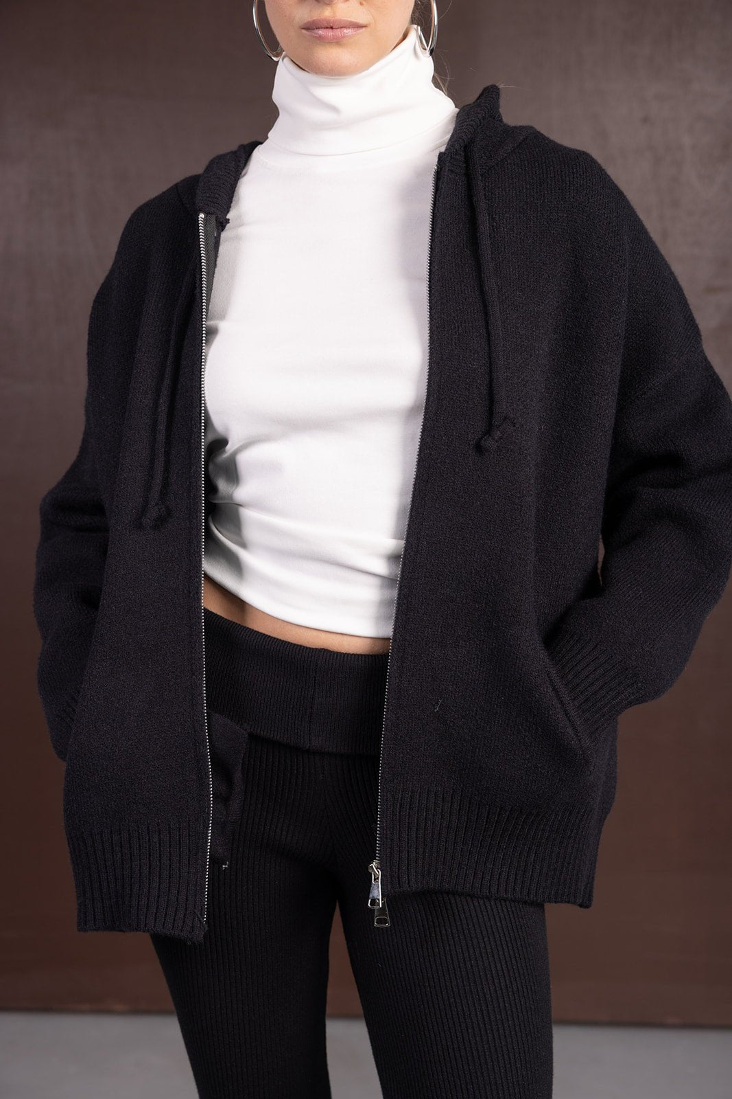 אישה עונדת עליונית קפוצ'ון סרוגה בצבע שחור, חולצה לבנה בגזרת גולף, ומכנסיים שחורים מחולקים, אופנה לנשים צעירות