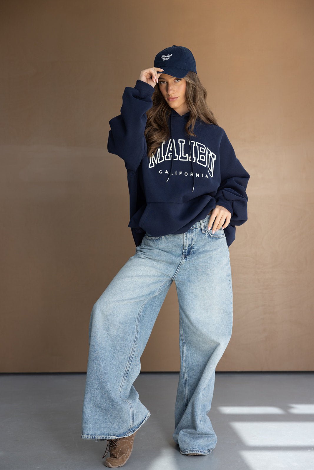 אופנת נשים: דוגמנית עם סווטשירט כחול MALIBU, מכנסי ג'ינס רחבים וכובע כחול