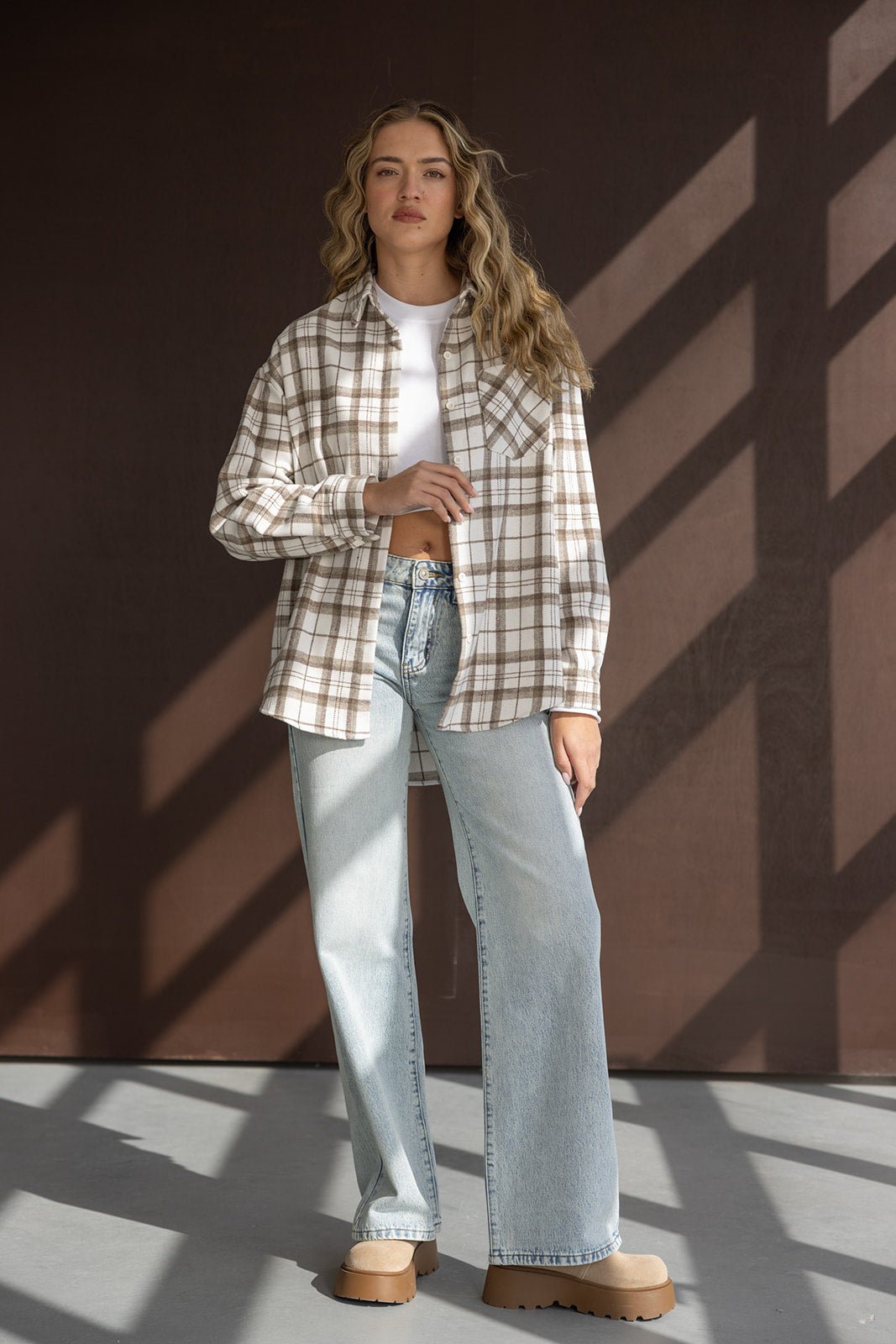 אישה צעירה לובשת חולצה משובצת בגווני בז' ולבן, טופ קצר לבן וג'ינס בגזרה רחבה, אופנת רחוב לנשים