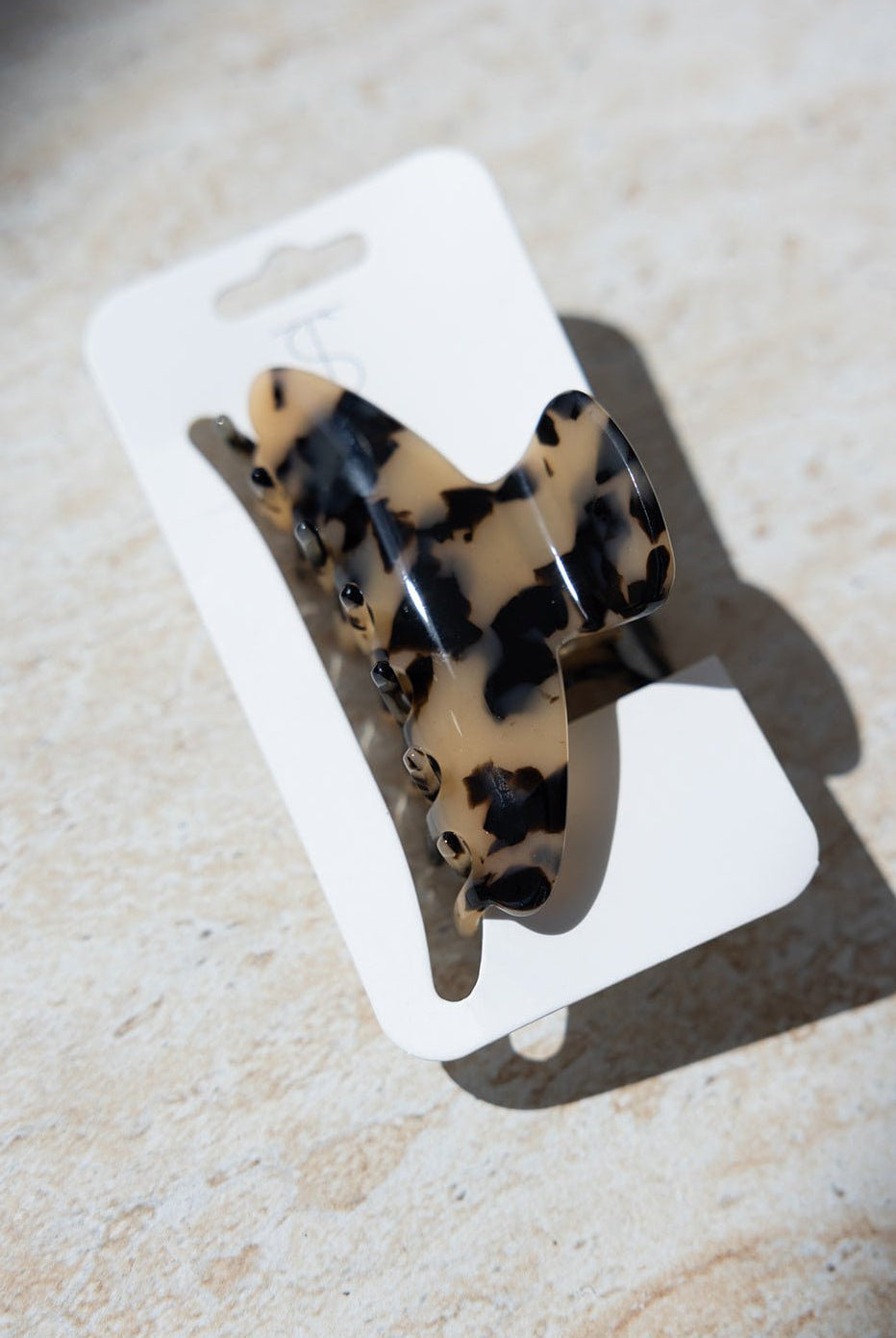 קליפס שיער בסגנון מנומר בגווני בז' ושחור, מונח על כרטיס קרטון לבן