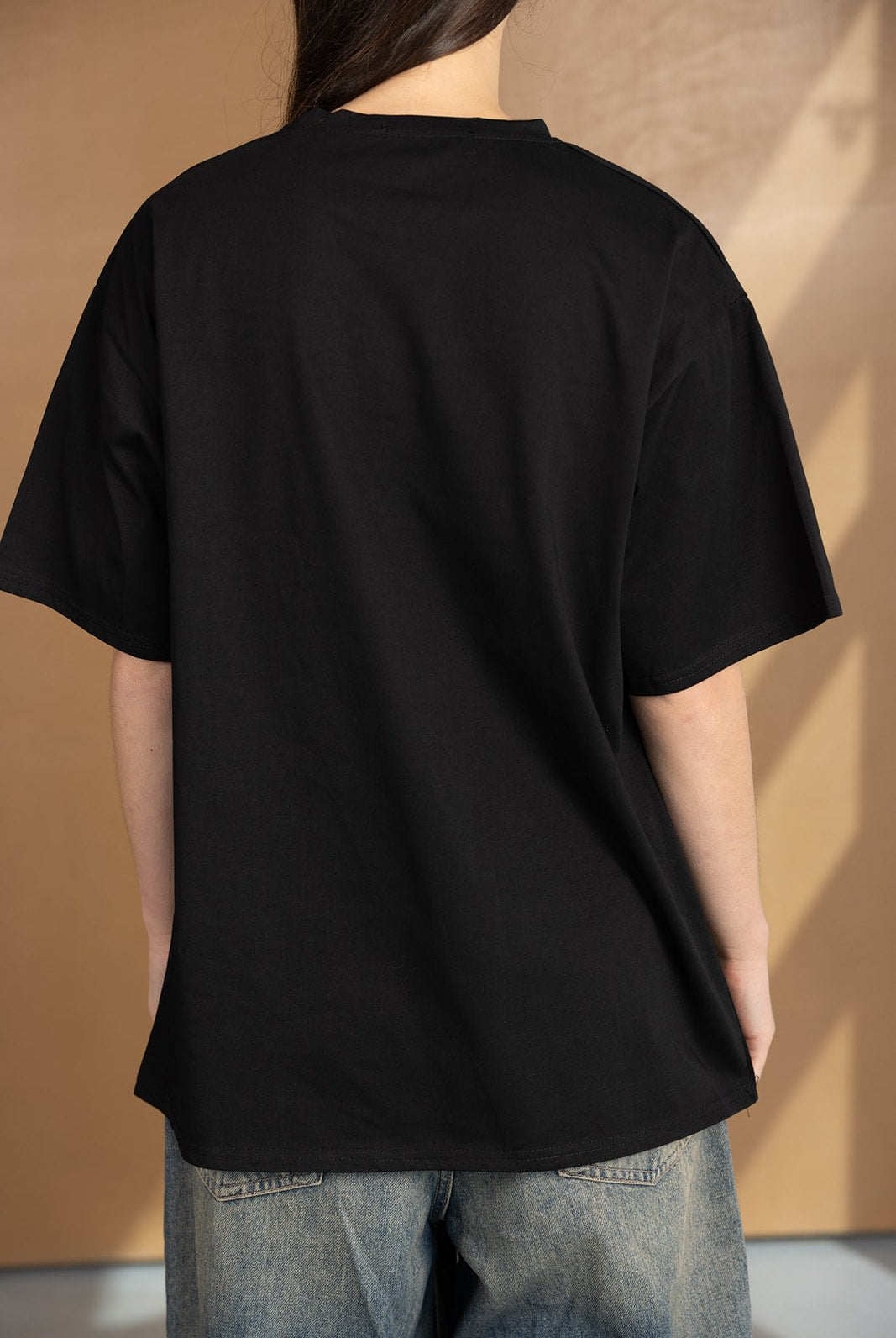 חולצת טי שירט שחורה לנשים בגזרה רחבה עם שרוולים קצרים, ג'ינס כחול, צילום מאחור