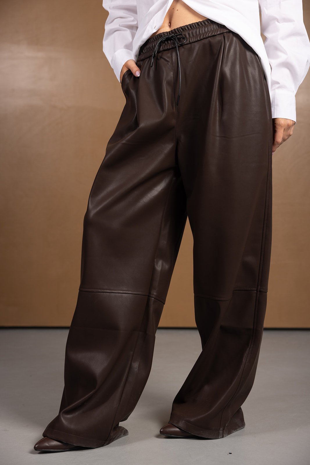 מכנסיים רחבים חומים דמוי עור אופנתיים לנשים, חולצה לבנה רקע ניטרלי