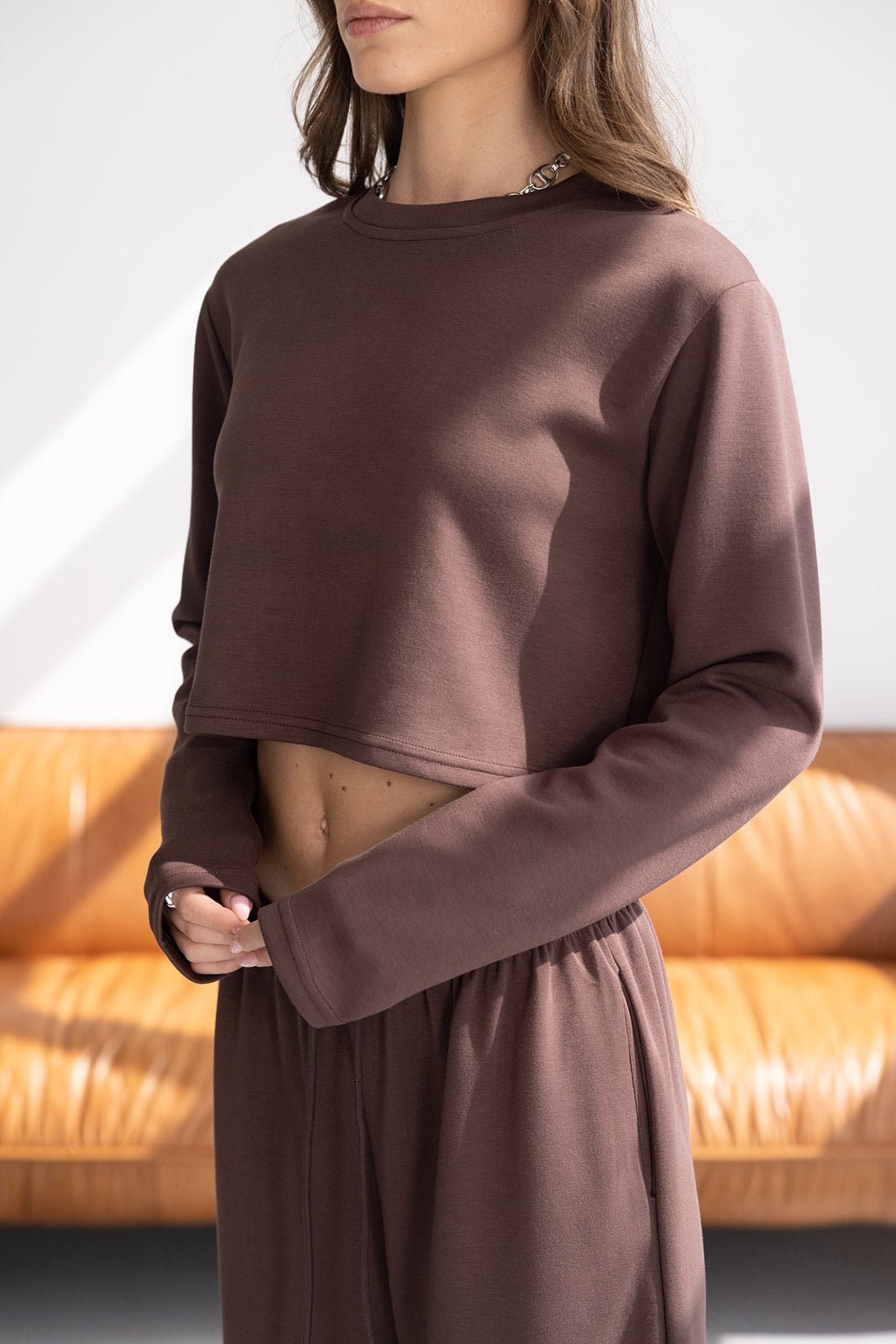 אישה לובשת סט טרנינג חום, חולצת קרופ שרוול ארוך ומכנסיים תואמים, אופנת נשים צעירה