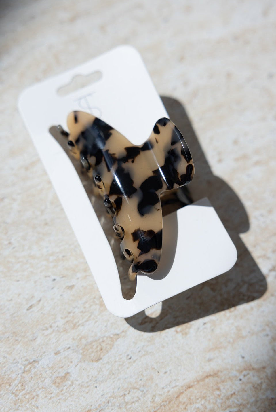 סיכת שיער קליפס מנומר בגווני בז' ושחור, מונחת על גבי קרטון לבן, צילום על רקע בהיר