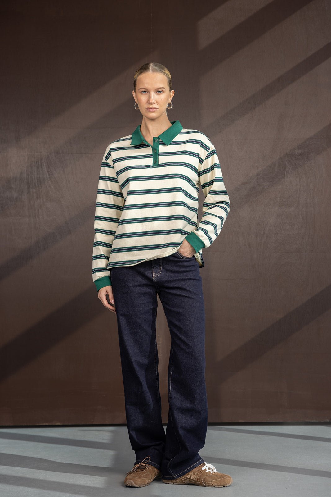 אישה לובשת חולצת פולו פסים ירוקה וכחולה עם ג'ינס כהה ונעלי סניקרס חומות, אופנת נשים קז'ואל