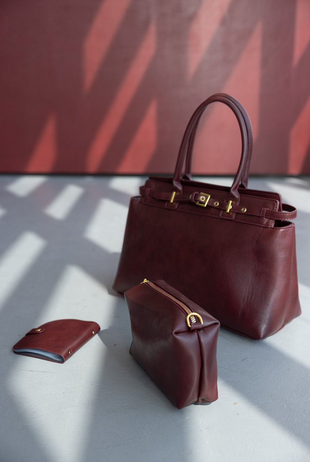 סט תיקי עור לנשים בצבע בורדו, כולל תיק יד, ארנק וקלאץ' אופנתי על רצפת בטון