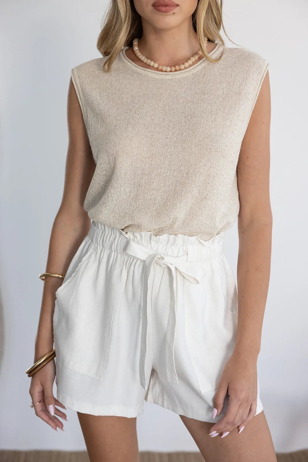 אישה לובשת גופיית בז' ושורטס קיץ לבנים עם קשירה, אופנת נשים קיץ