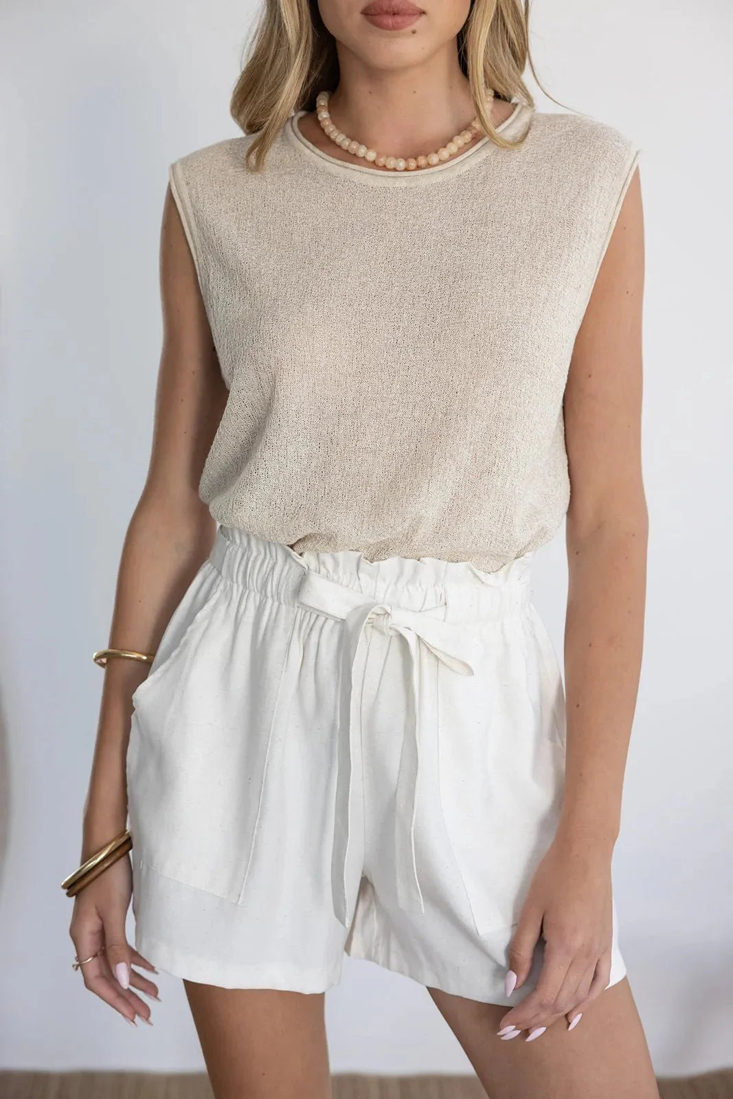 אישה לובשת גופיית בז' ושורטס קיץ לבנים עם קשירה, אופנת נשים קיץ