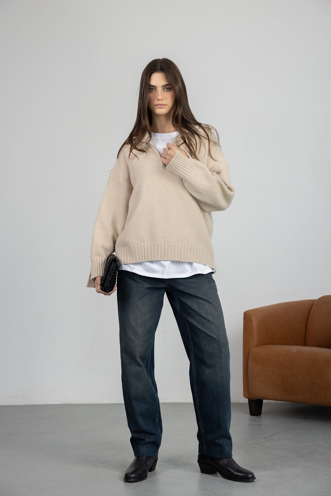 אישה עם סוודר בז', ג'ינס כהה, חולצה לבנה ונעלי עור שחורות, אופנה לנשים בסגנון קז'ואל