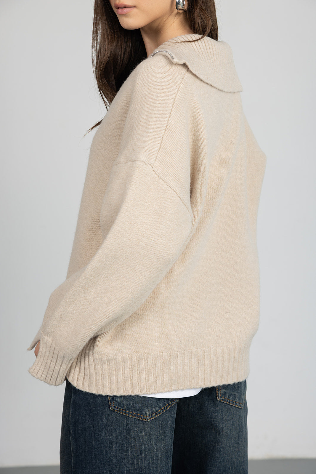 צעירה עם סוודר בז' בגזרה רחבה ומכנסי ג'ינס כהים, אופנה לנשים ונערות