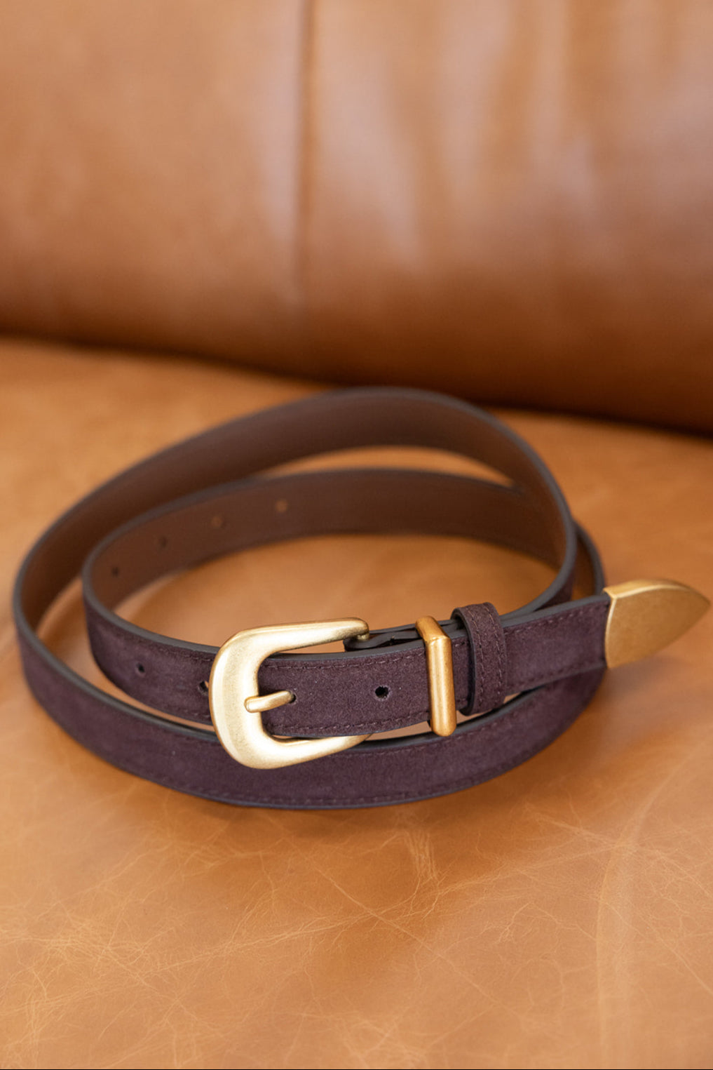 חגורת עור סגולה עם אבזם זהב על ספה חומה, אקססוריז אופנה לנשים