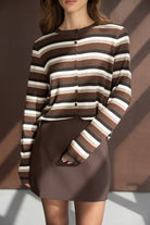 אישה לובשת חולצה עם פסים חומים ולבנים וחצאית חומה קצרה, ביגוד אופנתי לנשים