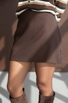 חצאית מיני חומה לנשים עם מגפיים חומים, חולצה פסים בצבעי חום ולבן, אופנה טרנדית לצעירות