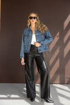 אישה עם ז'קט ג'ינס, גופיה לבנה, מכנסי עור שחורים רחבים ומשקפי שמש אופנתיים