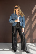 דוגמנית עם ג'קט ג'ינס, טופ לבן, מכנסי עור שחורים ומשקפי שמש אופנתיים בסגנון רחוב