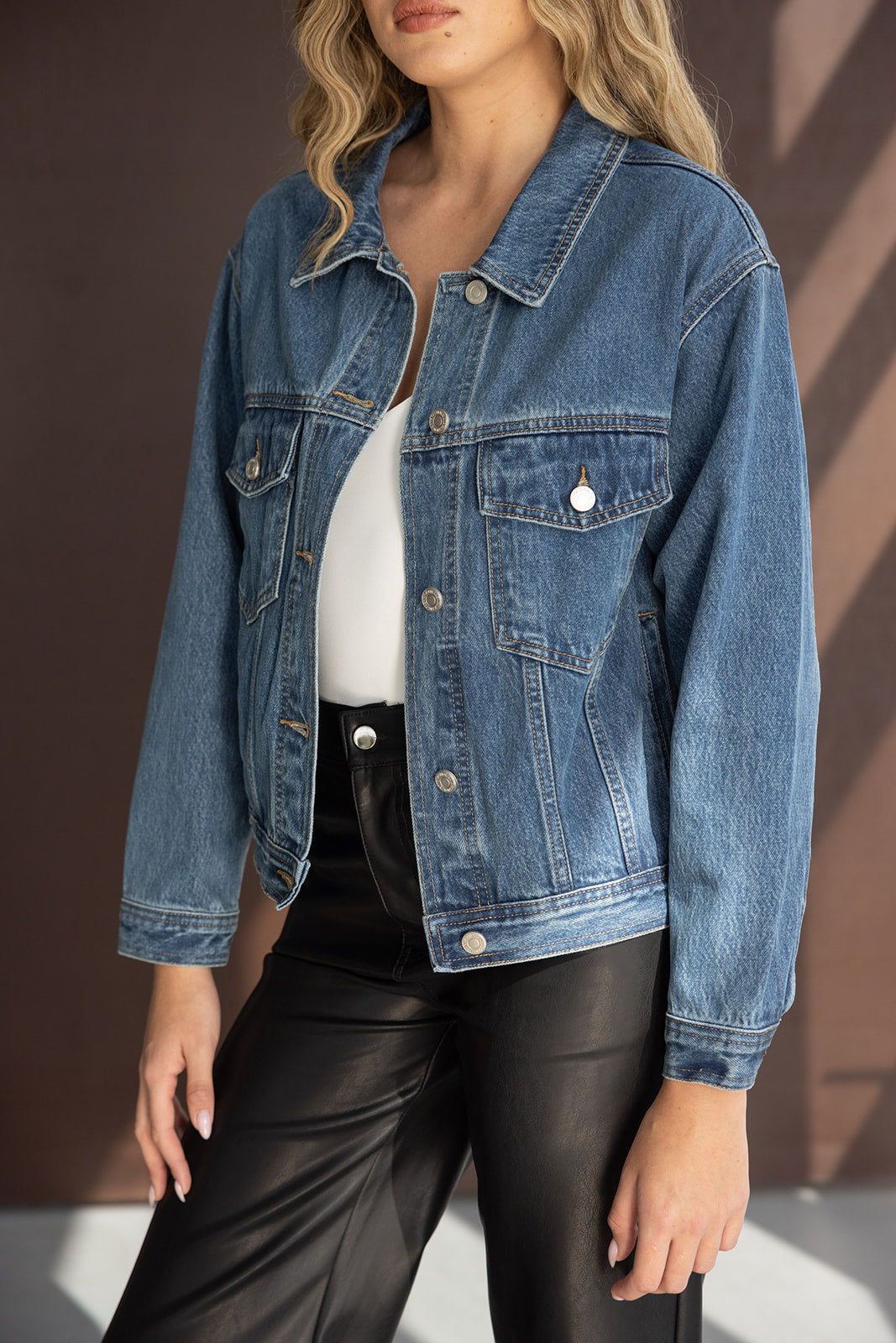 אישה לובשת ג'קט ג'ינס כחול על גבי חולצה לבנה ומכנסי עור שחורים, אופנת נשים עדכנית