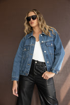 אישה עם ז'קט ג'ינס, גופיה לבנה, מכנסי עור שחורים ומשקפי שמש אופנתיים