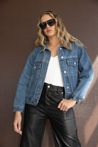 דוגמנית עם ג'קט ג'ינס לנשים, מכנסי דמוי עור שחורים וטופ לבן, לוק אופנתי לנערות