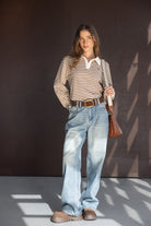 אישה לובשת חולצת פסים חומה ולבנה, ג'ינס בגזרה רחבה, חגורה ותיק צד חום, בגדי אופנה לנשים