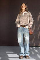 אופנת נשים, דוגמנית לובשת חולצת פסים חום-לבן ומכנסי ג'ינס רחבים, חגורה חומה ותיק כתף