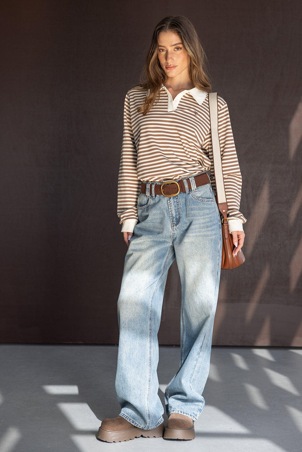 אישה לובשת חולצת פסים ארוכה בצבע חום ולבן, ג'ינס בגזרה רחבה ונעלי טרקטור חומות, לוק אופנתי לנשים
