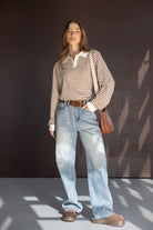 אישה לובשת חולצת פסים חומה ולבנה, ג׳ינס רחב, חגורה חומה ותיק צד חום, אופנת רחוב לנשים