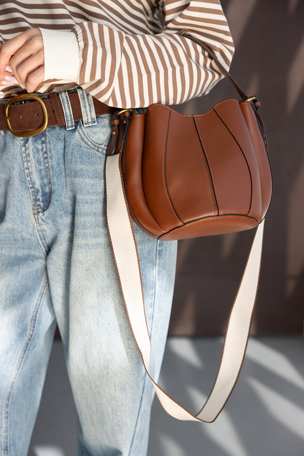 תיק צד חום מעור עם רצועה רחבה, חולצת סטריפס חומה וג’ינס בגזרה גבוהה לאופנת נשים