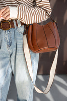 תיק צד חום מעור עם רצועה רחבה, חולצת סטריפס חומה וג’ינס בגזרה גבוהה לאופנת נשים