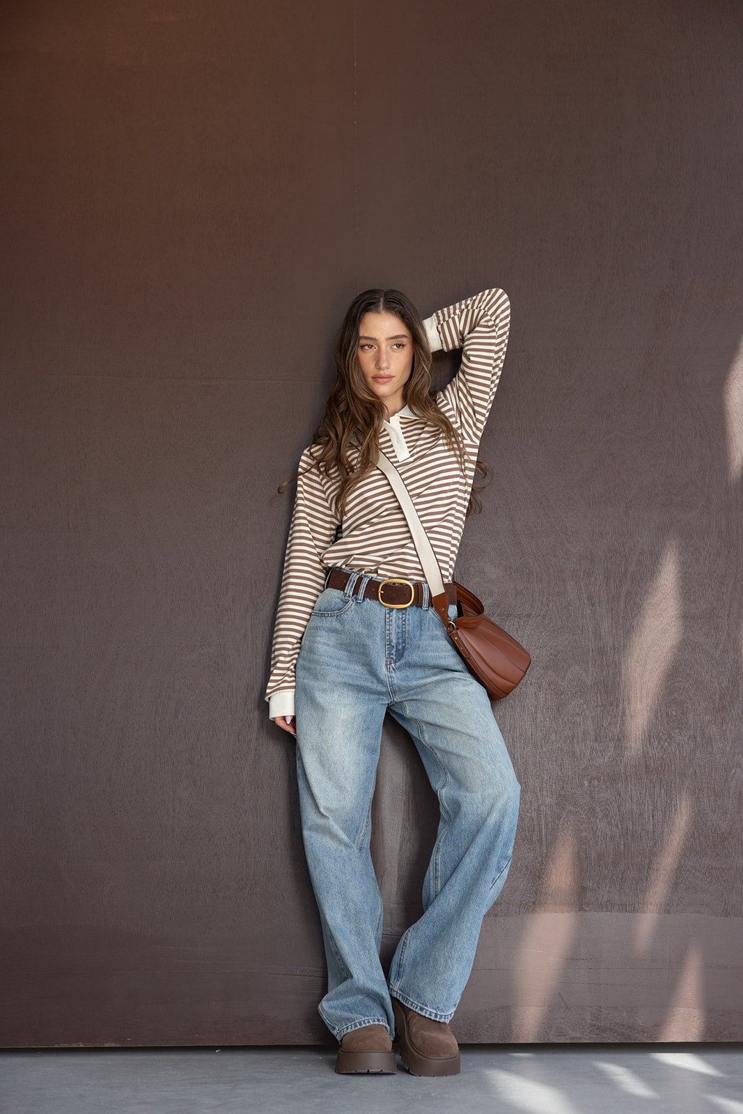 אישה עם חולצת פסים חומה ולבנה, ג'ינס גבוה רחב, מגפיים חומים ותיק צד, אופנת צעירות ישראלית