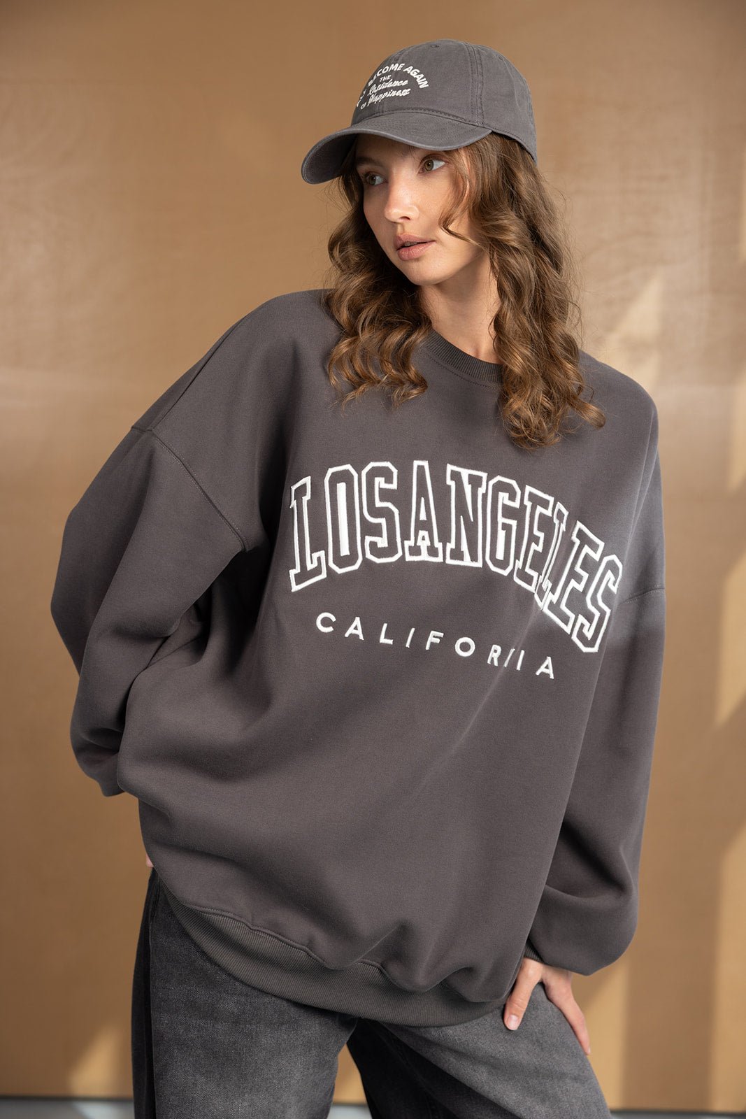 אישה לובשת קפוצ'ון אפור עם הדפס LOS ANGELES CALIFORNIA וכובע מצחייה אופנתי, צילומי אופנה עדכניים