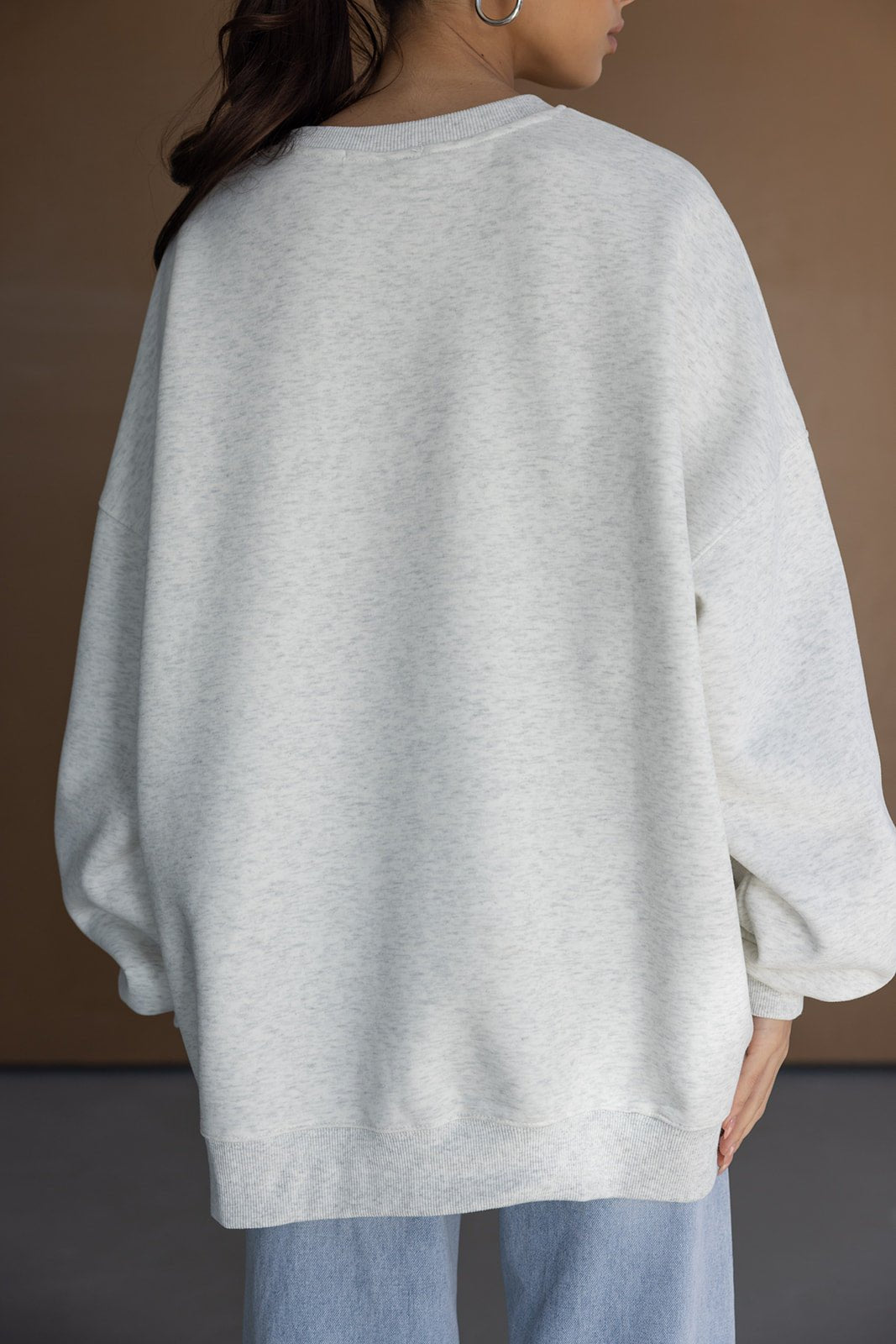 אישה לובשת סווטשירט אפור אוברסייז עם שרוולים רחבים ומכנסי ג'ינס, צילום מאחור, אופנת נשים