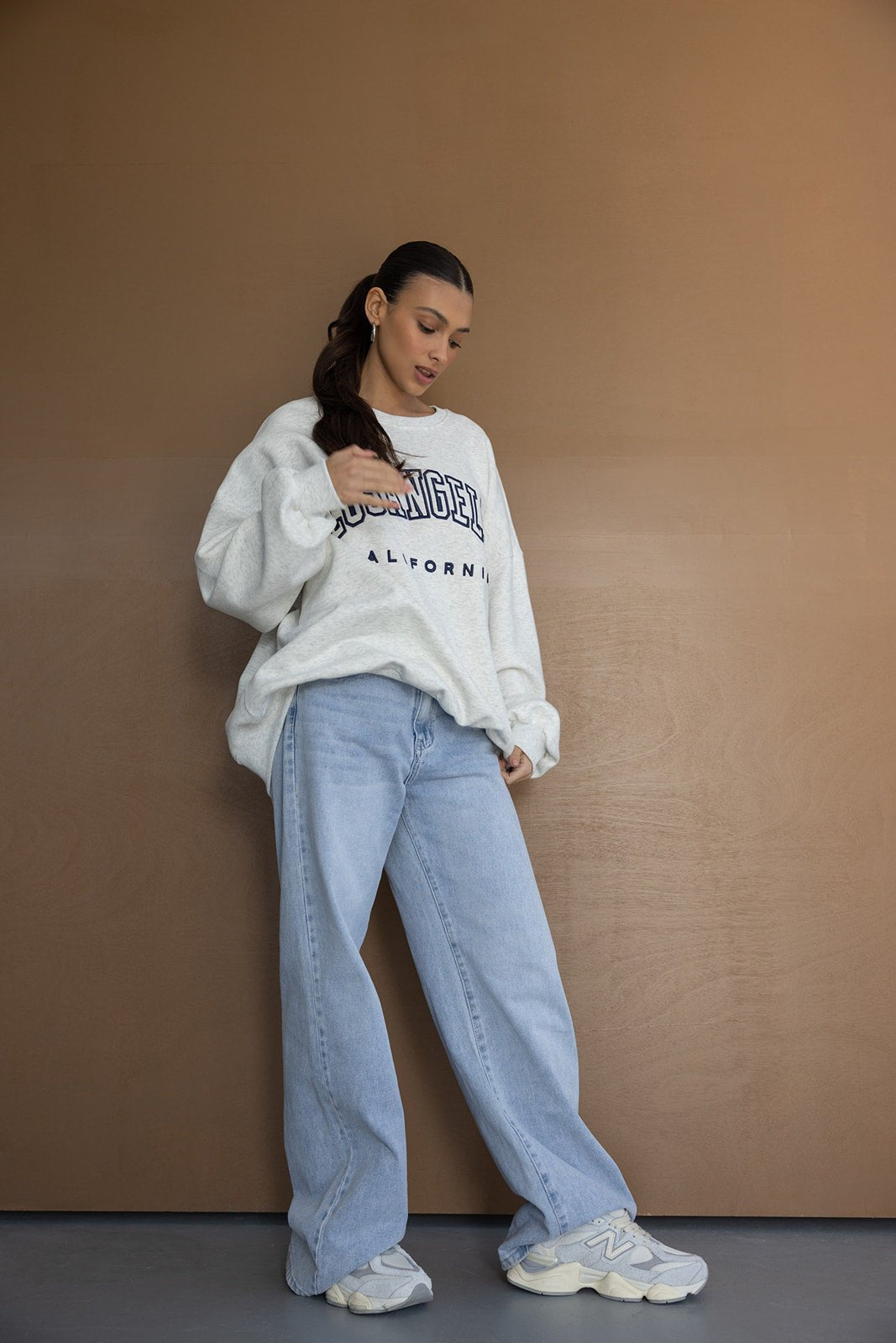 דוגמנית עם סווטשירט אפור עם כיתוב, ג'ינס רחב ונעלי סניקרס אופנתיות לנשים