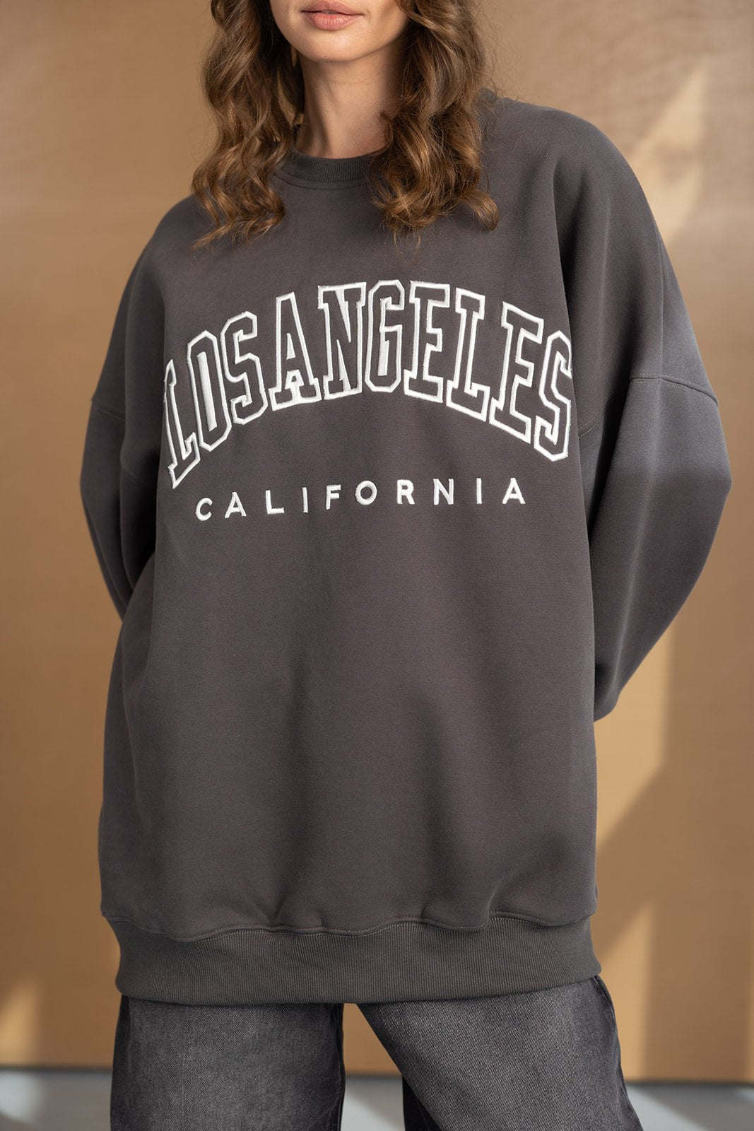 אישה לובשת סווטשירט אופנתי אפור עם כיתוב 'LOS ANGELES CALIFORNIA', אופנת נשים נוחה
