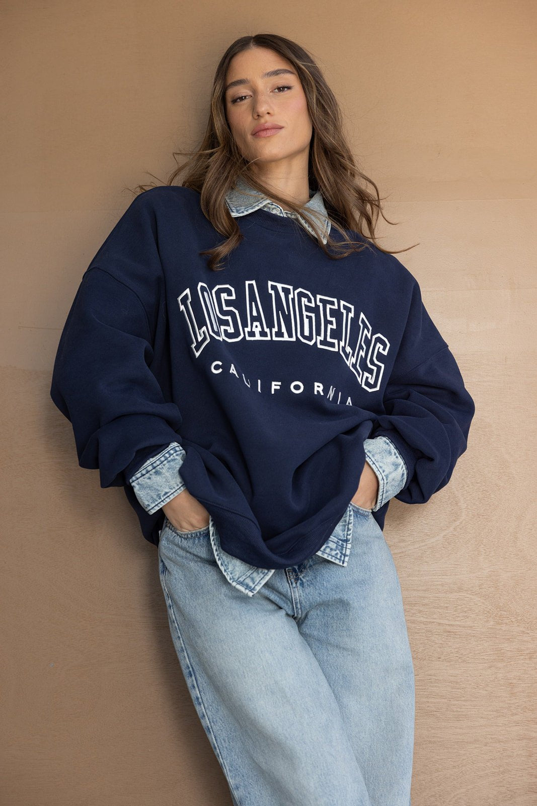 אישה לובשת סווטשירט כחול כהה עם כיתוב Los Angeles ומכנסי ג'ינס אופנתיים לצעירות