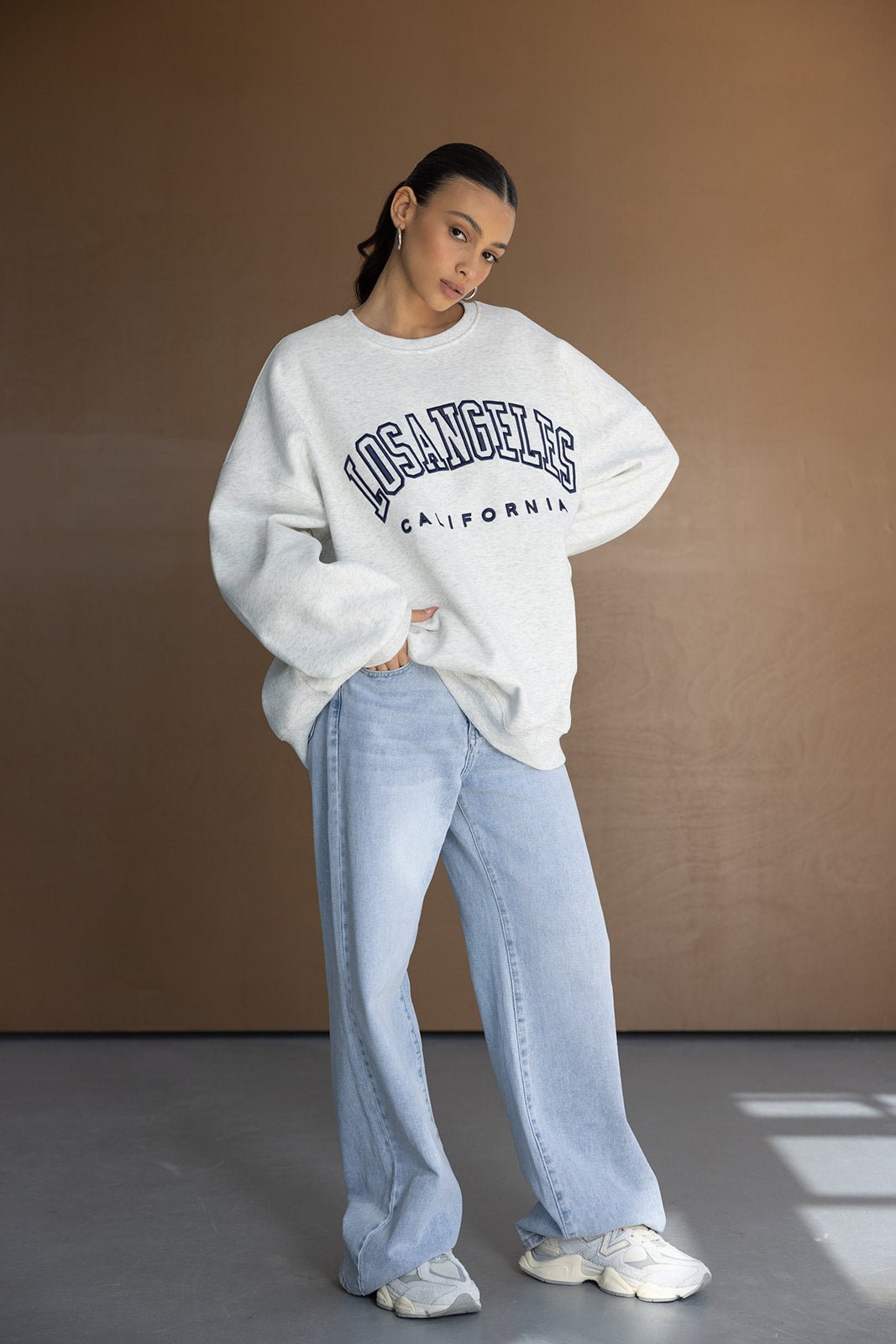 אופנת נשים, דוגמנית עם סווטשירט אפור 'LOS ANGELES', ג'ינס רחב ונעלי סניקרס לבנות
