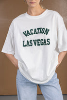 חולצת טי לבנה לנשים עם כיתוב ירוק VACATION LAS VEGAS, גזרה רחבה, ג'ינס בהיר