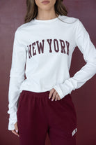 אישה לובשת סווטשירט לבן עם כיתוב NEW YORK ומכנסיים בורדו, אופנת נשים צעירה