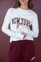 אישה לובשת חולצת טרנינג לבנה עם כיתוב NEW YORK ומכנסי טרנינג בורדו אופנתיים