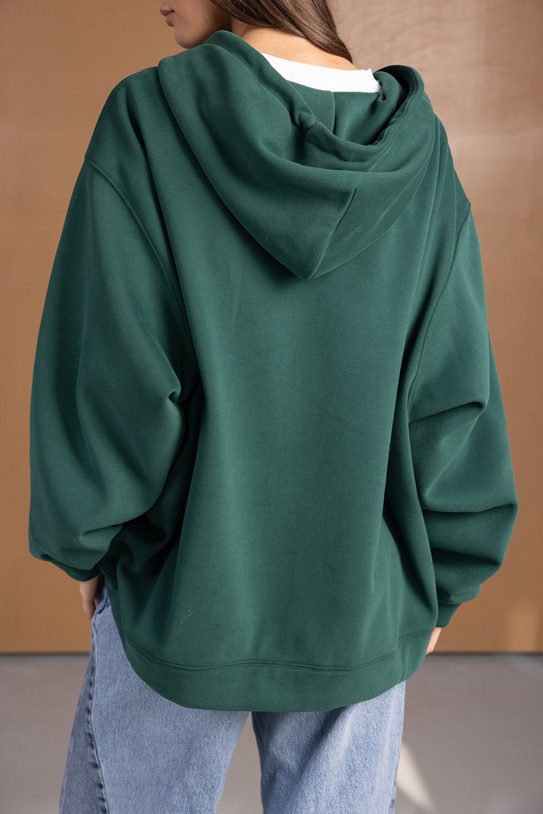 קפוצ׳ון ירוק לנשים עם גזרה רחבה, שרוולים ארוכים, ושילוב ג׳ינס אופנתי ברקע ניטרלי