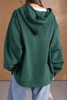 קפוצ׳ון ירוק לנשים עם גזרה רחבה, שרוולים ארוכים, ושילוב ג׳ינס אופנתי ברקע ניטרלי