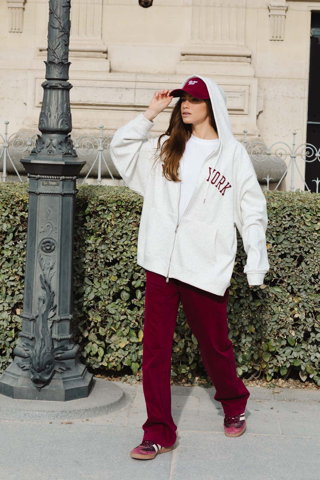 אישה צעירה בלבוש רחוב אופנתי, סווטשירט אפור עם קפוצ'ון, מכנסי טרנינג אדומים וכובע מצחייה, הלבשה לנשים