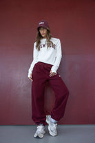 דוגמנית בסטייל ספורטיבי לובשת חולצת ניו יורק לבנה ומכנסי טרנינג בורדו, כובע ותספורת רפויה