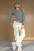 אישה עם חולצת פסים ארוכה, מכנסי טרנינג לבנים, כובע מצחייה ונעלי ספורט