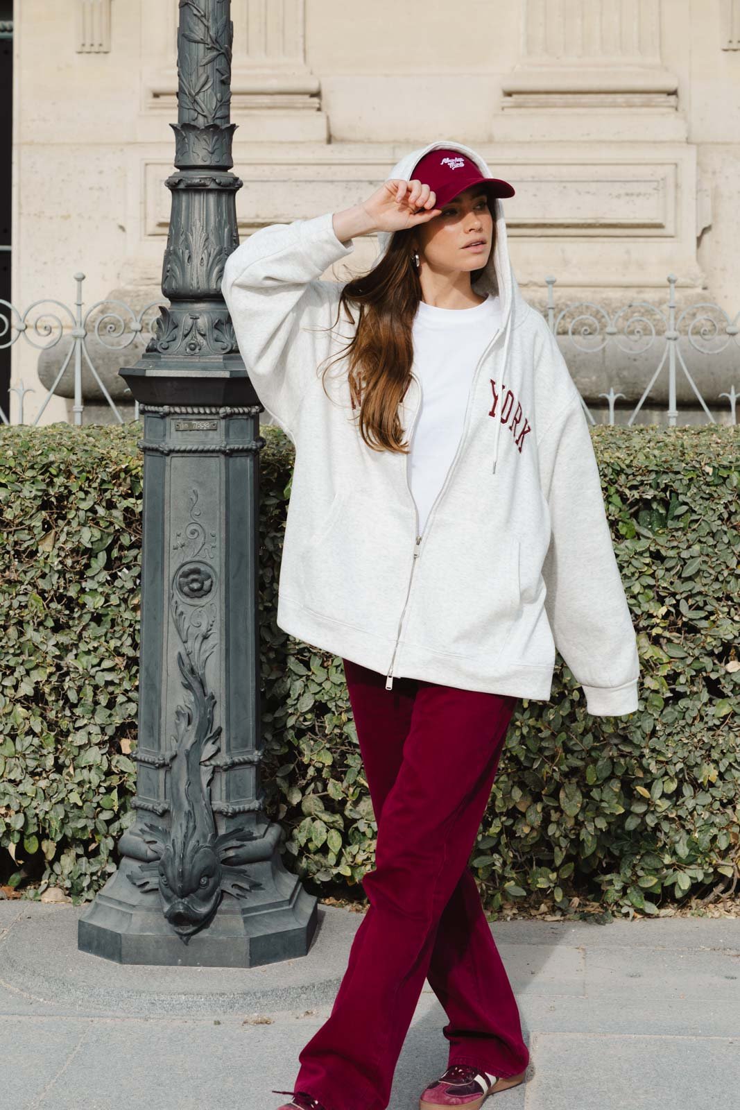 אישה עם קפוצ׳ון אפור, חולצה לבנה ומכנסיים בורדו, אופנת רחוב לנשים