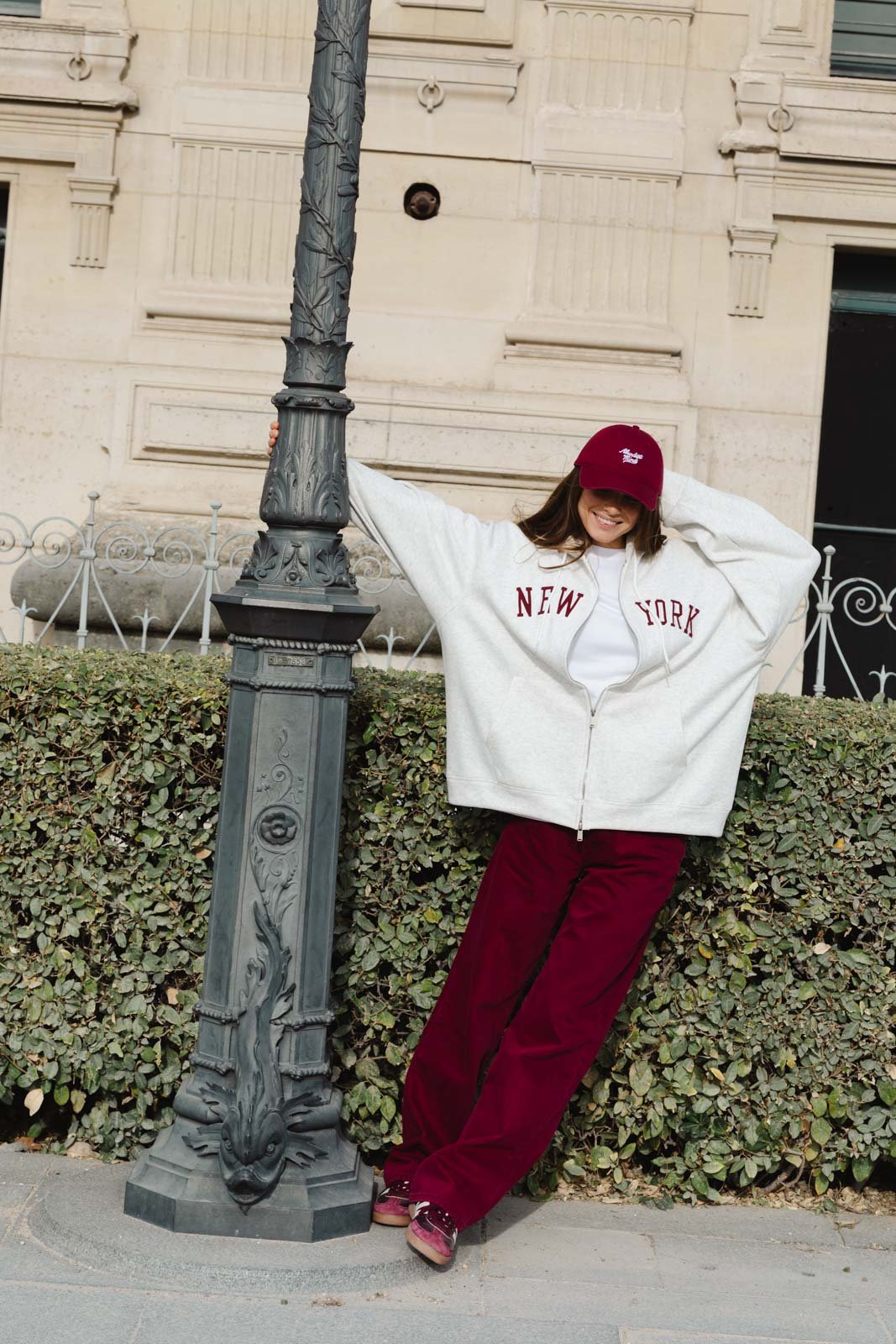 אישה אופנתית עם קפוצ'ון לבן כיתוב ניו יורק, כובע ובגדים בורדו, בסטייל רחוב עירוני