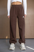 מכנסי טרנינג חומים לנשים עם גומי במותן, חולצת בטן לבנה ונעלי סניקרס אופנתיות